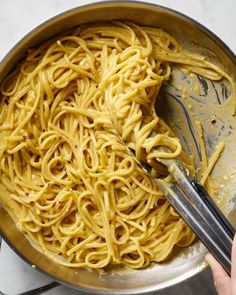 someone is stirring spaghetti in a pan with tongs