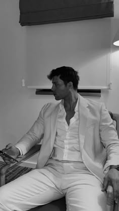 a man sitting in a chair wearing a white suit and holding a cell phone to his ear