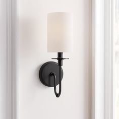 a black wall mounted light with a white shade on it's side and a window in the background