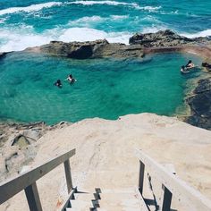 two people swimming in the ocean near some rocks and stairs with steps leading up to them