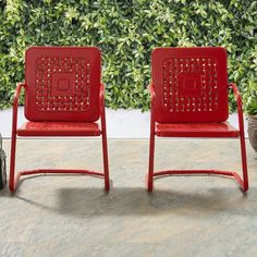 two red chairs sitting next to each other in front of a green wall and potted plant