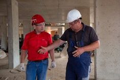 two men in hard hats and overalls standing next to each other