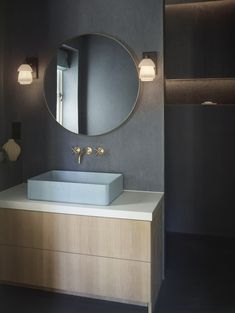 a bathroom sink with a round mirror above it and lights on the wall behind it