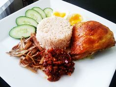 a white plate topped with rice, meat and veggies next to cucumbers