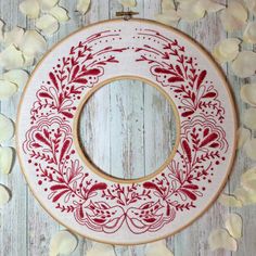 a red and white embroidered wreath on a wooden surface with petals around it, surrounded by shells