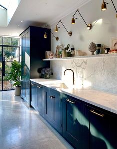 a kitchen with blue cabinets and marble counter tops, gold lighting fixtures and potted plants