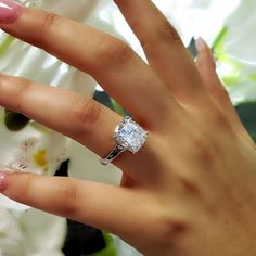 a woman's hand with a diamond ring on her finger and flowers in the background