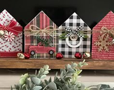 three wooden houses decorated with christmas decorations and bows on top of a shelf next to a potted plant