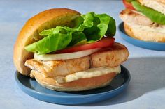 a chicken sandwich with lettuce and tomato on a blue plate next to another sandwich