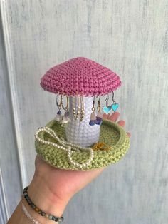 a hand holding a small knitted mushroom on top of a green tray with beads