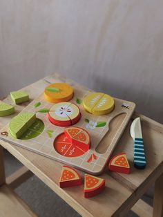 a child's wooden cutting board with fruits and vegetables on it sitting on top of a table