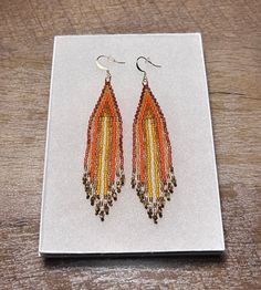 These earrings are handmade with Japanese myuki beads and accent beads on the ends of the fringe. The colors include various shades of orange, cream white and brown. Orange Fringe Dangle Earrings, Handmade Orange Long Drop Earrings, Orange Fringe Tassel Earrings For Gift, Handwoven Orange Beaded Earrings For Gift, Handwoven Orange Beaded Earrings As Gift, Orange Beaded Fringe Dangle Earrings, Orange Teardrop Beaded Earrings With Ear Wire, Brown Beaded Earrings With Fringe, Orange Handwoven Dangle Beaded Earrings