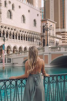 a woman standing on a railing looking at the water in front of a large building