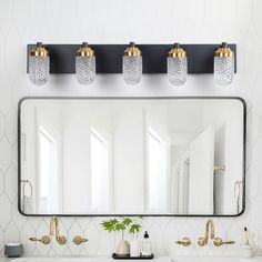 a bathroom vanity with three lights and a large mirror above it, along with two gold faucets