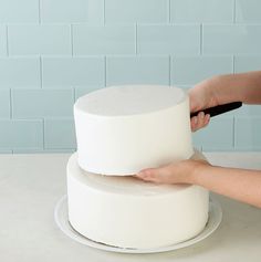 a person is decorating a cake with white frosting on a table in front of a blue tile wall