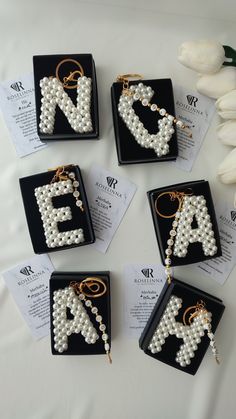 four letters made out of pearls are on display in black trays next to white tulips