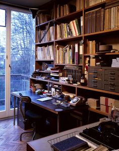 a home office with lots of books on the shelves and a desk in front of a large window