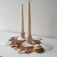 two candles with shells and sand on the table