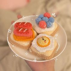 a person holding a plate with three small crocheted food items on top of it