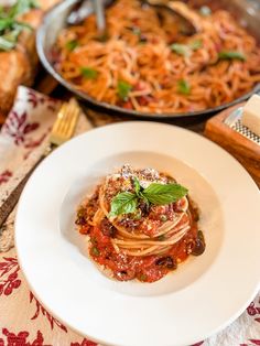 a white plate topped with spaghetti and sauce next to other dishes on a wooden table