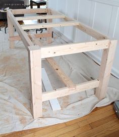 a wooden table being constructed in the middle of a room with white walls and wood flooring