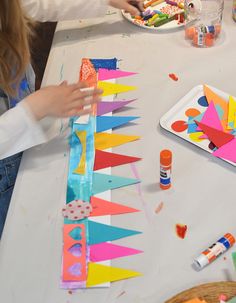 two children are making colorful kites out of construction paper at a table with craft supplies