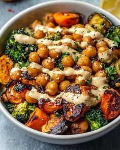 a white bowl filled with broccoli and chickpeas covered in sauce next to lemon wedges