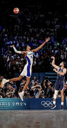 two men playing basketball in front of a crowd with cameras on the sidelines watching