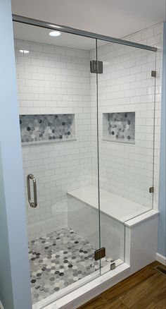 a walk in shower sitting next to a white tiled wall and wooden floored floor