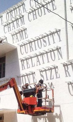 a man on a cherry picker is painting the side of a large white building