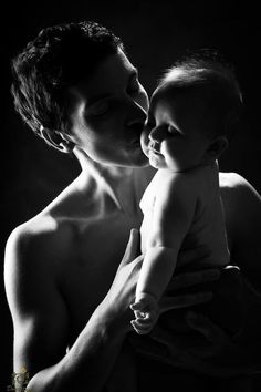 a man holding a baby in his arms and kissing it's face with the other hand