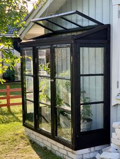 a small greenhouse in front of a white house with black trim and glass doors on the side