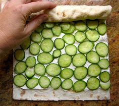 a person holding a piece of bread with cucumbers on it