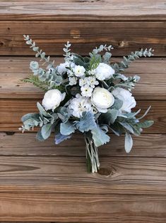 a bouquet of white flowers and greenery on a wooden surface with wood planks