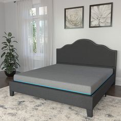 a bed with a gray headboard and blue piping on the bottom half is in a white room