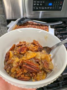 a bowl filled with food sitting on top of an oven next to a person holding a spoon