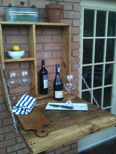 a wooden table with wine glasses and bottles on it next to a brick wall in front of a window