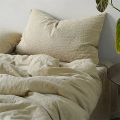 an unmade bed with two pillows and a plant on the side table next to it