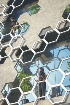 two people standing on the side of a building with glass windows and hexagonal structures