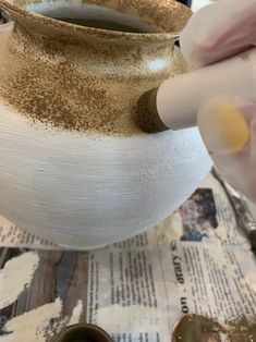 a person is painting a white vase with gold flecks