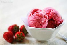 three scoops of strawberry ice cream in a white bowl with strawberries on the side