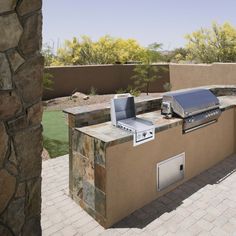 an outdoor bbq with grill and sink in the middle of a patio surrounded by rocks