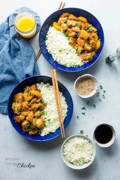 two blue plates filled with rice and chicken next to cups of orange juice on a white table