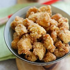 a bowl filled with fried food sitting on top of a wooden table next to a green towel