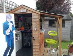 a small wooden shed with a man holding a cat in it's arms and standing next to the bar