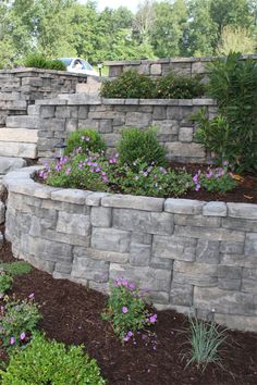 a stone wall and flower bed with purple flowers