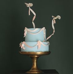 a three tiered blue cake with pink ribbon on top and two birds flying over it