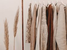 several sweaters are hanging on a rack in front of a white wall and some dried grass