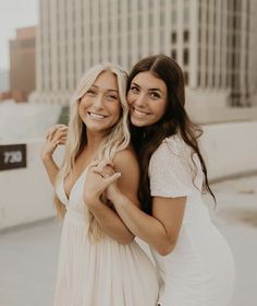 two beautiful young women standing next to each other in front of a tall building smiling at the camera