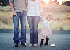 two adults and a child standing in the middle of an empty road with grass behind them